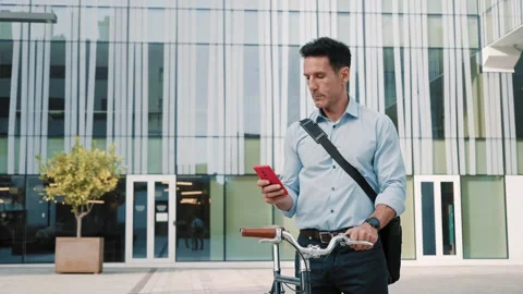 Businessman with bicycle using red cell phone app outside the office 動画素材 306658928