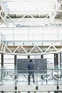 Businessman at blackboard with complex equations in atrium Stock Photos