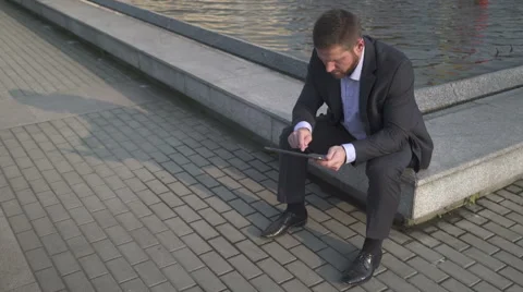 Businessman browsing tablet, sitting on wall. 库存影片 52754947