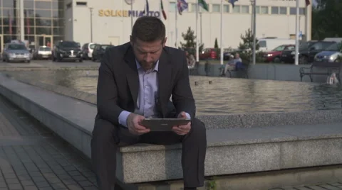 Businessman browsing tablet, sitting on wall. Vidéo 52755182