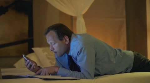 Businessman calculating data from documents on smartphone lying on bed  HD Stock Footage 45442286