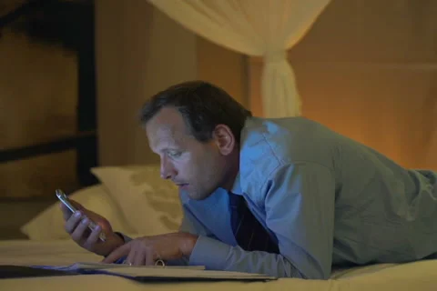Businessman calculating data from documents on smartphone lying on bed  NTSC Stock Footage 45442394
