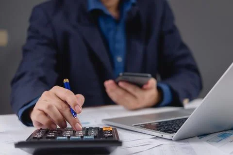 Businessman calculating financial data using calculator and holding mobile .. Stock Photos