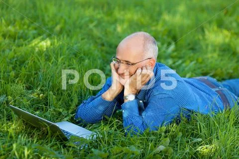 Businessman chatting online on laptop while lying on grass Stock Photos
