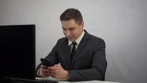 Businessman chatting in smartphone while working. A young man in a suit sits in Stock Footage 230289332