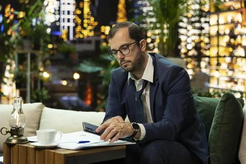 Businessman checking phone notification while reviewing reports at night Foto stock