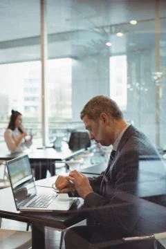 Businessman checking time while using laptop in cafeteria Fotos de archivo
