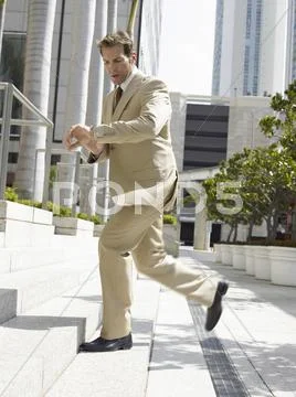 Businessman Climbing Office Steps While Looking At Wristwatch Stock Photos