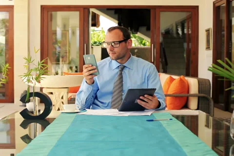 Businessman comparing data on smartphone and tablet by table at home NTSC Stock Footage 40881301