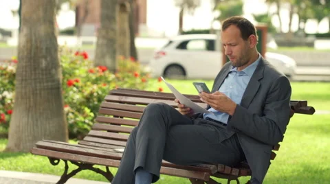 Businessman comparing data on smartphone and documents at the city bench HD Stock Footage 43399211