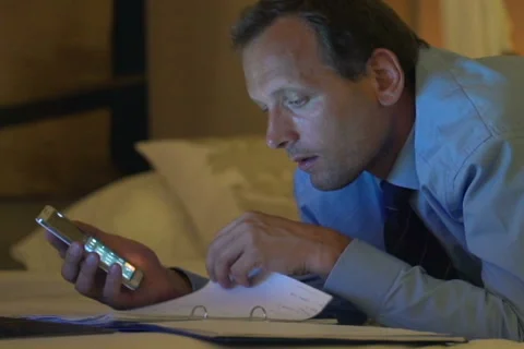 Businessman comparing data on smartphone and documents on bed at home NTSC Stock Footage 45500414