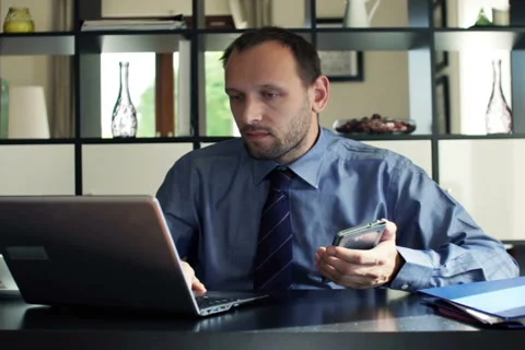 Businessman comparing data on smartphone and laptop in the office NTSC Stock Footage 45677433