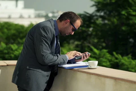 Businessman comparing data on smartphone and documents, standing on terrace NTSC Stock Footage 46214134