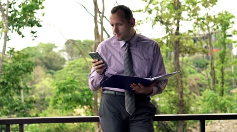 Businessman comparing data on smartphone and documents standing on terrace Stock Footage 53093172