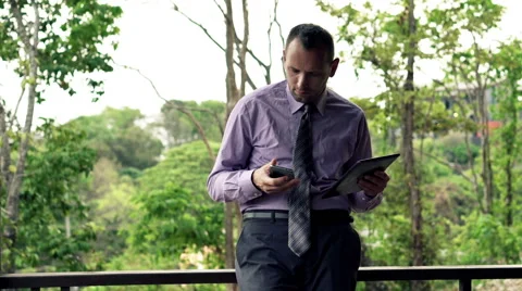 Businessman comparing data on smartphone and tablet computer standing on terrace Stock Footage 53093755