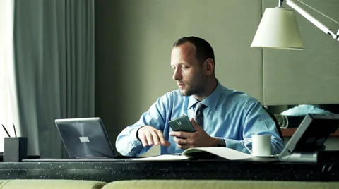 Businessman comparing data on smartphone, laptop and documents sitting in office Stock Footage 54692973