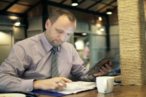 Businessman comparing data on tablet and documents in cafe NTSC Stock Footage 49699898
