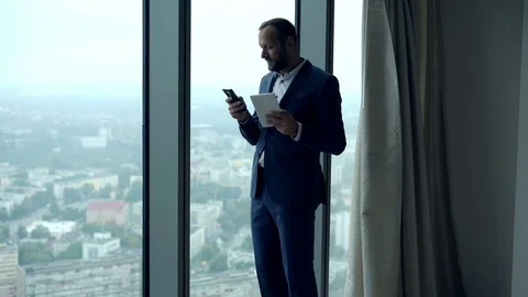 Businessman comparing data on tablet computer and smartphone by window in office Stock Footage 81325036