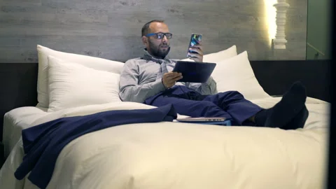 Businessman comparing data on tablet computer and smartphone on bed, 4k Stock Footage 86597817