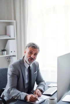 Businessman with computer sitting at the table in an office, making notes. Stock Photos