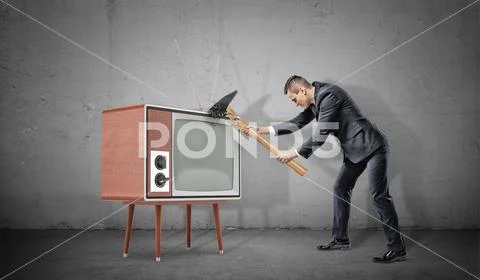 A businessman on concrete background fails to smash an old retro TV set with a Stock Photos
