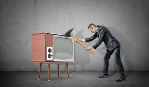 A businessman on concrete background fails to smash an old retro TV set with a Stock Photos