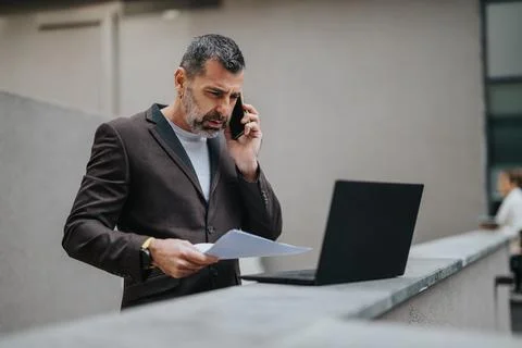 Businessman conversing on the phone while analyzing documents outside an office 写真素材