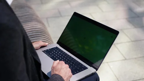 A businessman in a dark jacket is sitting on a bench, holding a laptop on his Stock Footage 282246085