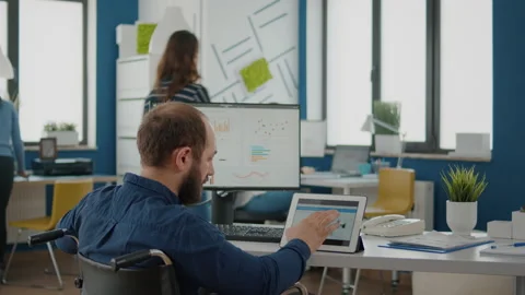 Businessman with disabilites using computer and tablet comparing graphs Stock Footage 154357931
