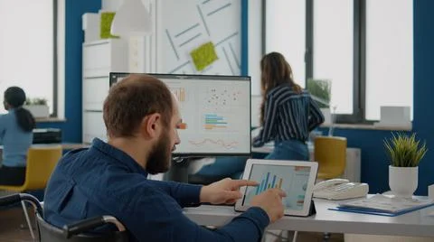 Businessman with disabilites using computer and tablet comparing graphs Foto stock