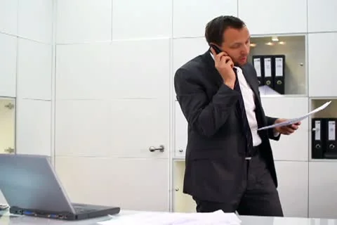Businessman with documents talking on cellphone in modern office NTSC Video stock 10744526