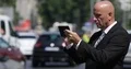 Businessman in Downtown on a Street with Crowded Traffic Text Using Cellphone 4k or 4k+ Resolution