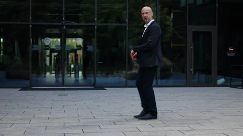 A businessman dressed in dark jacket and white shirt is dancing near glass Stock-Footage 281396013