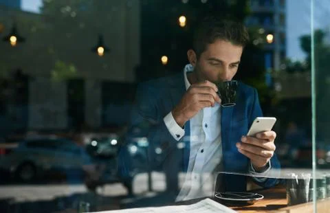 Businessman drinking coffee and checking his cellphone in a cafe Stock Photos