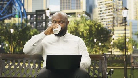 Businessman drinking coffee cup while using laptop on park bench Stock Photos