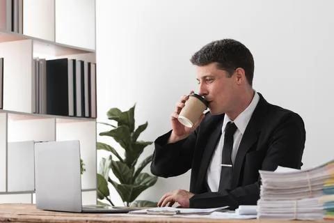 Businessman drinking coffee while working at desk with laptop, concept of break Stock Photos