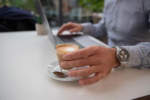A businessman drinks coffee while working on his laptop, close-up of his hand Foto stock