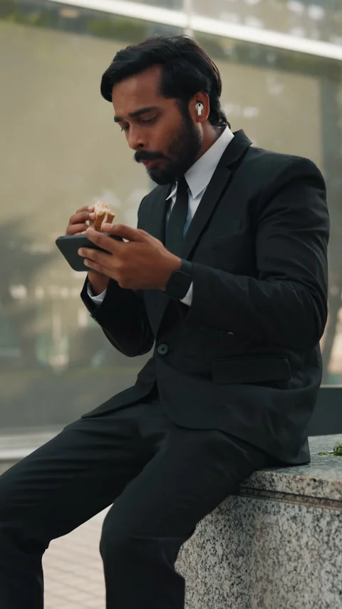 Businessman eating snack while looking at screen of phone Stock Footage 303736501