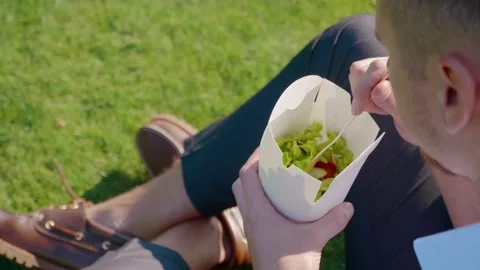 Businessman eats vegetables with paper ecological packaging with a wooden fork Stock Footage 130486884