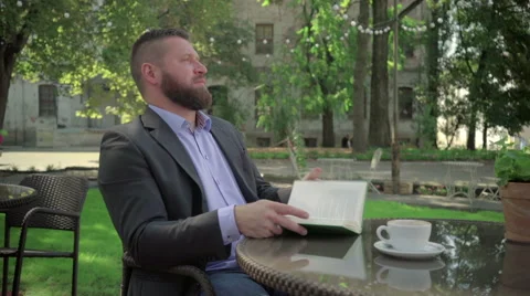 Businessman ends reading book during coffe break. Outdoor. Steadicam shot. 库存影片 65362849