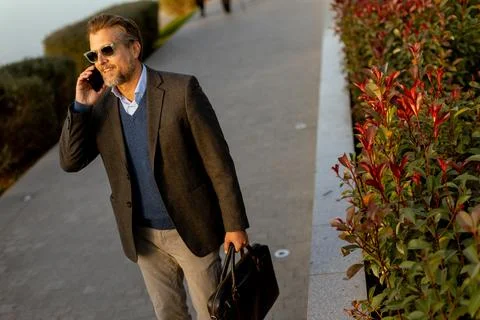 Businessman engaged in important call while walking along a scenic waterfro.. Stock Photos