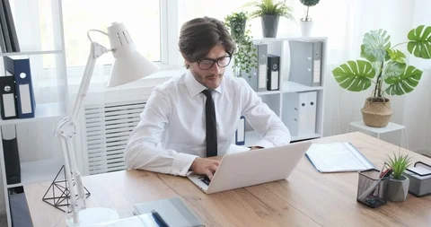Businessman examining document while using laptop at office Stock Footage 117702224