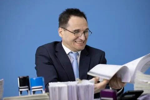 Businessman flips thick stack of accounting records amidst piles of paper Stock Photos