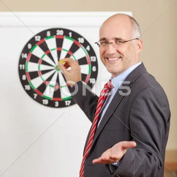Businessman gesturing while holding dart attached to target on f Stock Photos