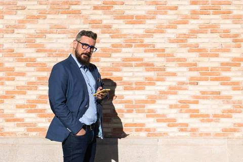Businessman in glasses looking at camera while using a smartphone outdoors Stock Photos