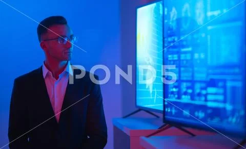 The businessman in glasses standing near big displays with graphs Stock Photos