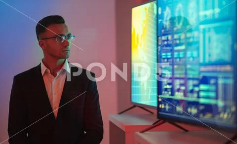 The businessman in glasses standing near big displays with graphs Stock Photos