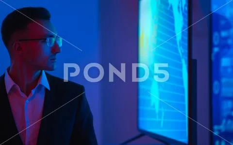 The businessman in glasses standing near screens with graphs Stock Photos