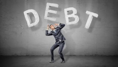 A businessman on a grey background cowers under large concrete letters making a Stock Photos