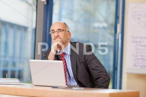 Businessman with hand on chin looking away at desk Stock Photos